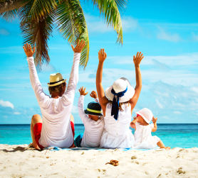 Famille portant des chapeaux et  assise sur la plage, les bras en l'air.